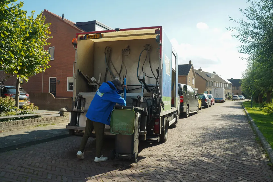 Medewerker brengt een container naar de reinigingswagen.